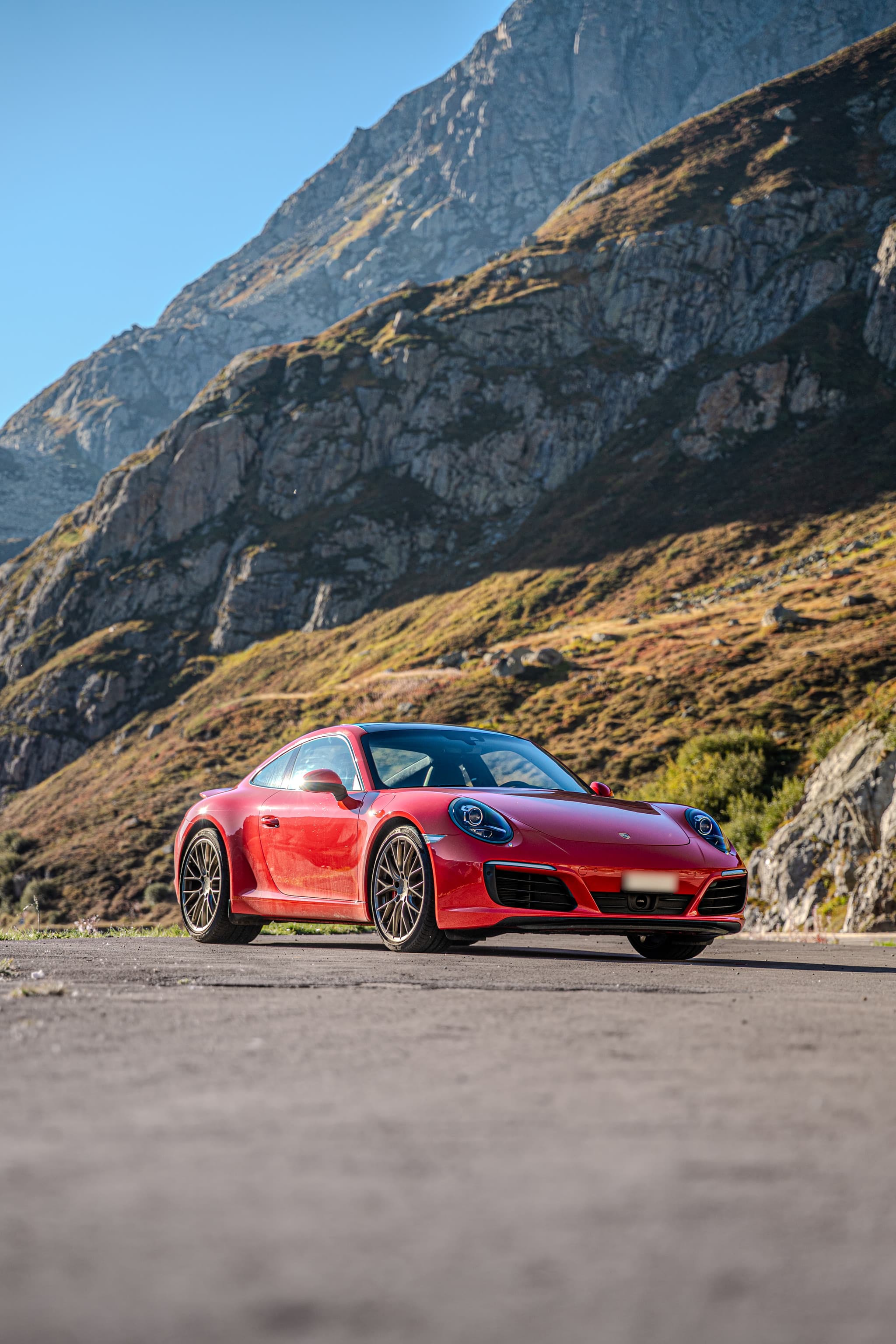Roter Porsche 911 Carrera S Coupé, Ansicht von schräg vorne auf einer Passstrasse unter hohen Felswänden