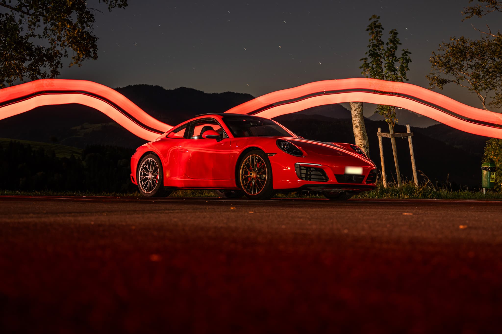 Roter Porsche 911 Carrera S Coupé, nachts vor einer geschwungenen roten Lichtspur